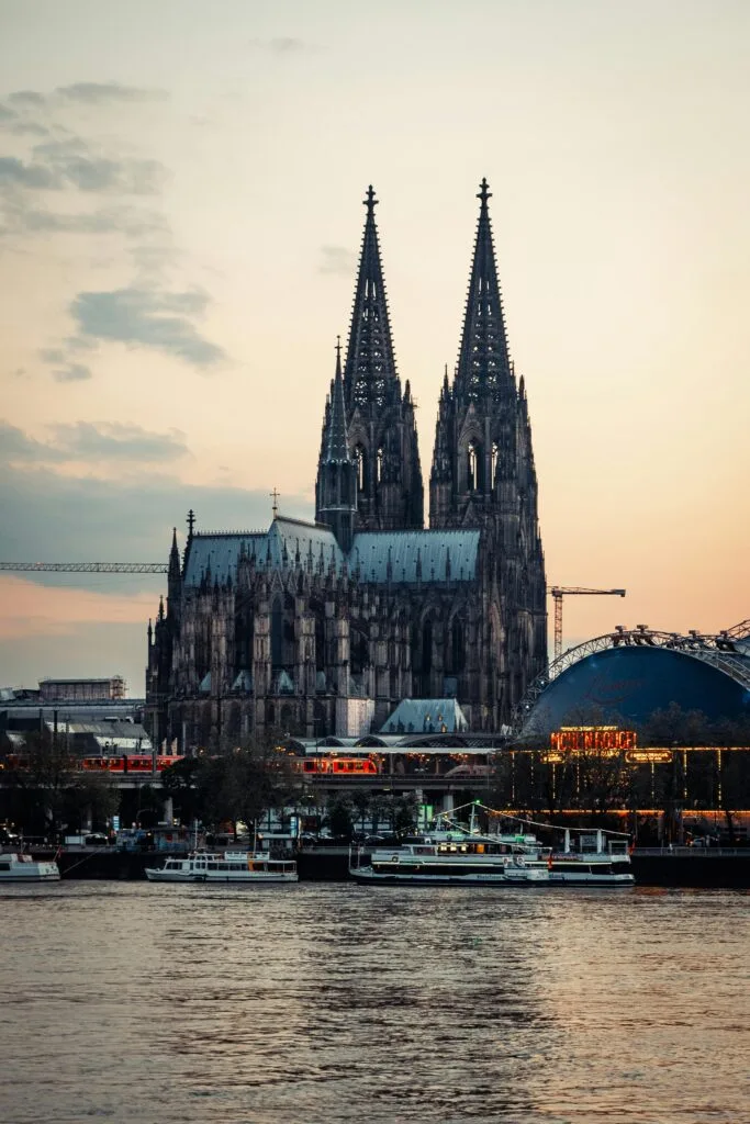 Cologne Cathedral and Hohenzollern Bridge at sunset with riverboats on the Rhine in Cologne, Germany