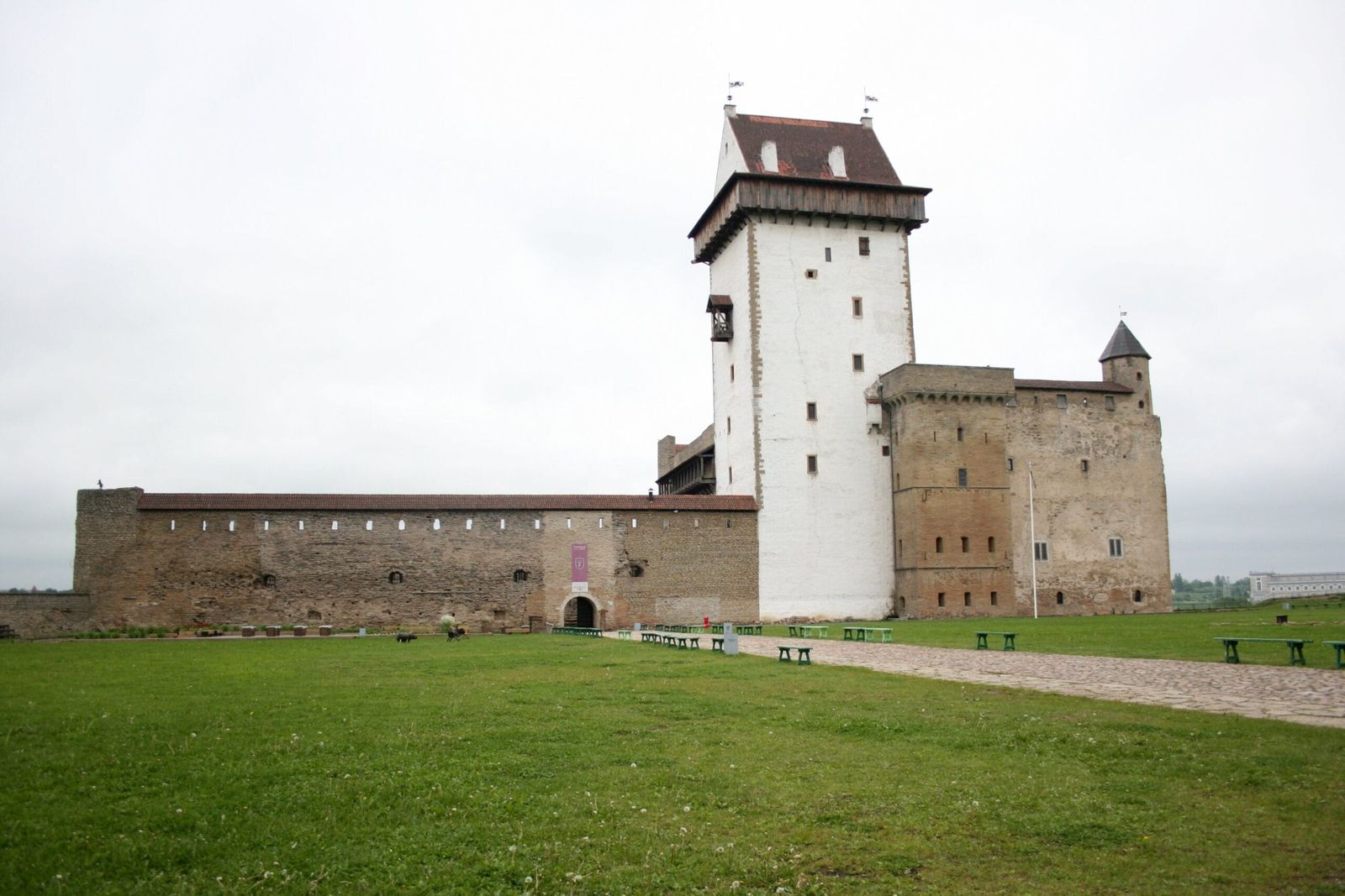 "Narva Castle in Estonia, a historic medieval fortress with a tall white tower, stone walls, and green courtyard, showcasing its rich cultural heritage and defensive architecture