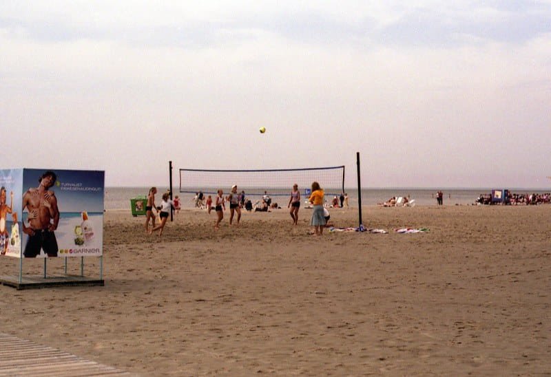People playing beach volleyball on a sandy shore with a calm sea in the background