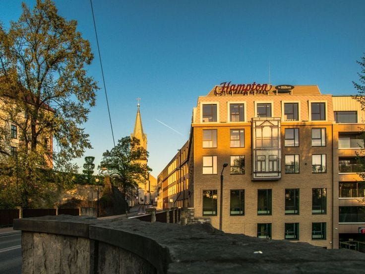 Hampton by Hilton hotel building in a European city with historic architecture, church tower, and sunset lighting