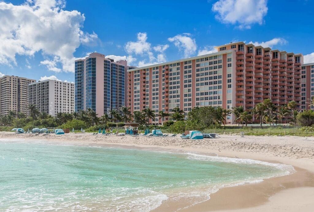 Beachfront view of Triton Towers Miami Beach with turquoise ocean, sandy shore, and high-rise condos under a blue sky