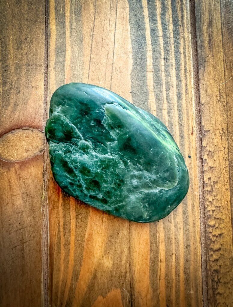 Close-up of a polished green Big Sur jade stone resting on a wooden surface, showcasing its natural texture and rich color.