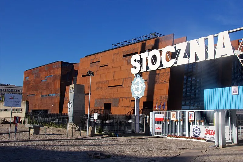 Exterior view of the European Solidarity Centre in Gdańsk, Poland, showing the historic shipyard gate and rust-colored architectural design under a clear blue sky
