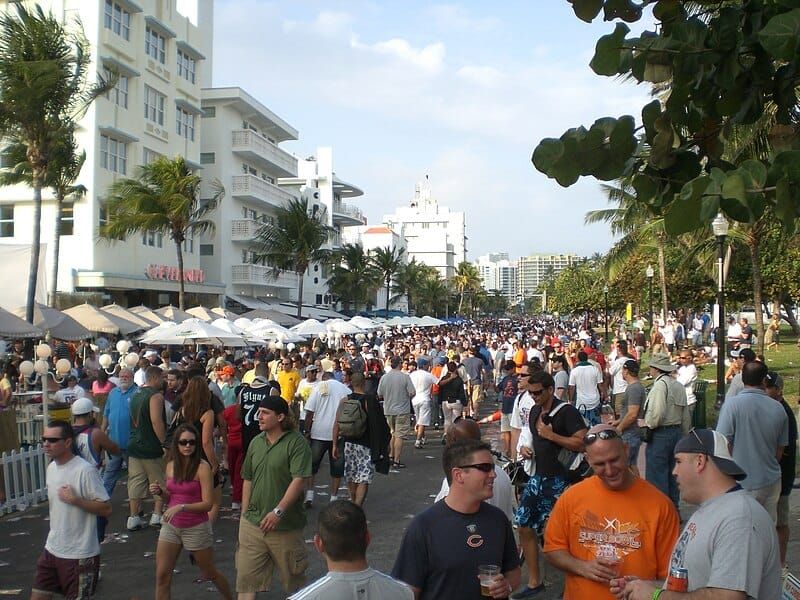 Crowds enjoying a lively outdoor event on Ocean Drive, Miami Beach, during Super Bowl XLI, with Art Deco buildings, palm trees, and festive street vendors