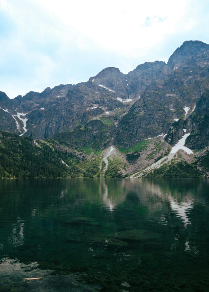 Tranquil morning at Morskie Oko Lake with crystal-clear water, rugged rocks, and mist rolling over the Tatra Mountain peaks in southern Poland.