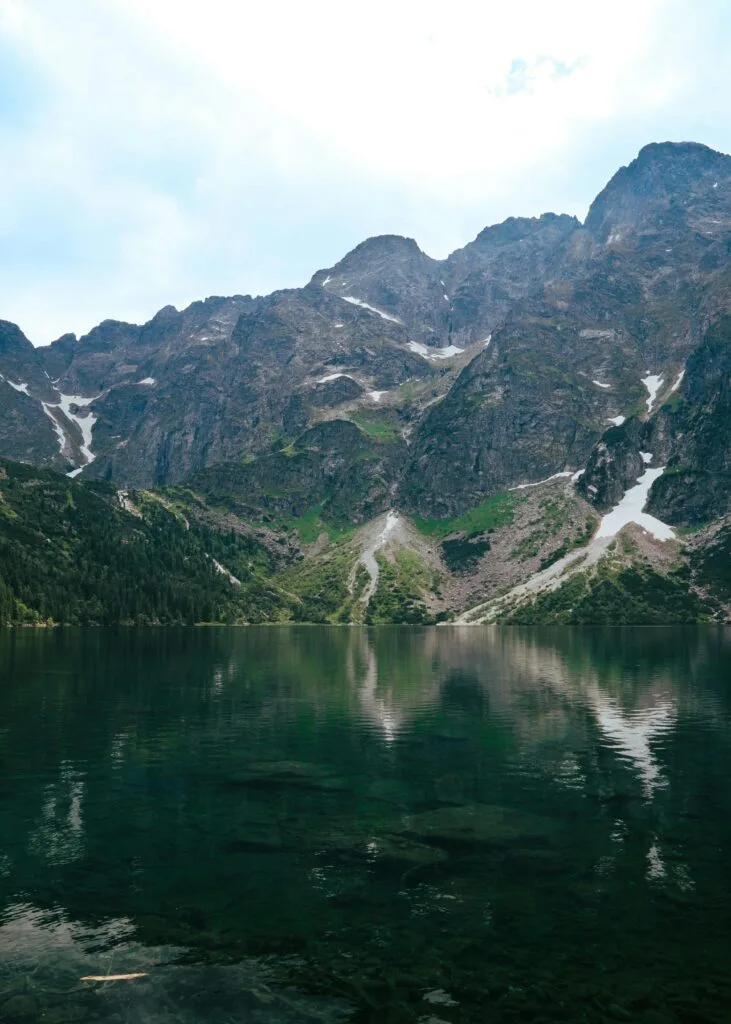 Tranquil morning at Morskie Oko Lake with crystal-clear water, rugged rocks, and mist rolling over the Tatra Mountain peaks in southern Poland.
