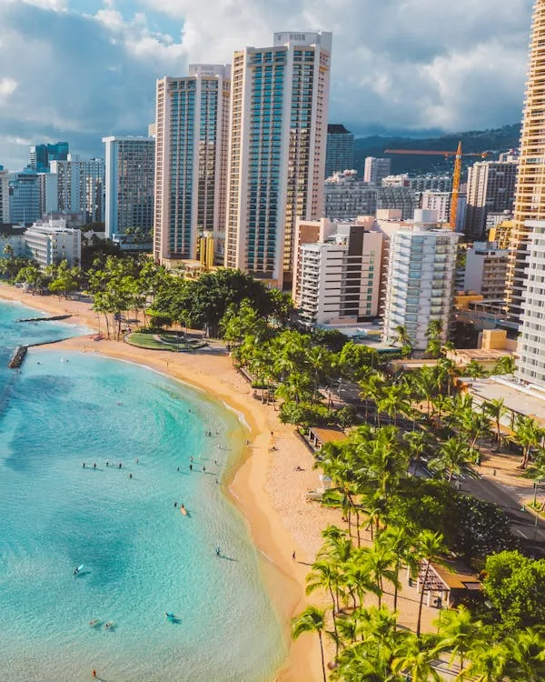 A scenic view of the best beaches in Honolulu, showcasing golden sands and clear blue waters with Mirasol Towers in the background