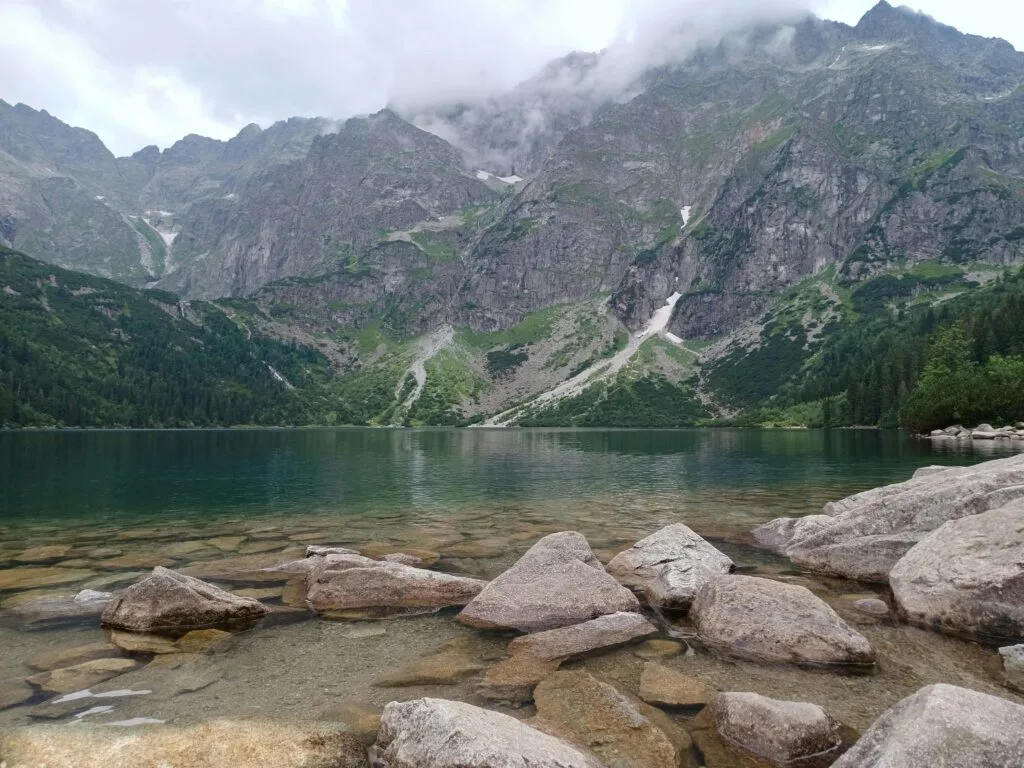 Scenic view of Morskie Oko Lake in the Tatra Mountains, Poland, with clear water, rocky shoreline, and misty mountain peaks in the background.