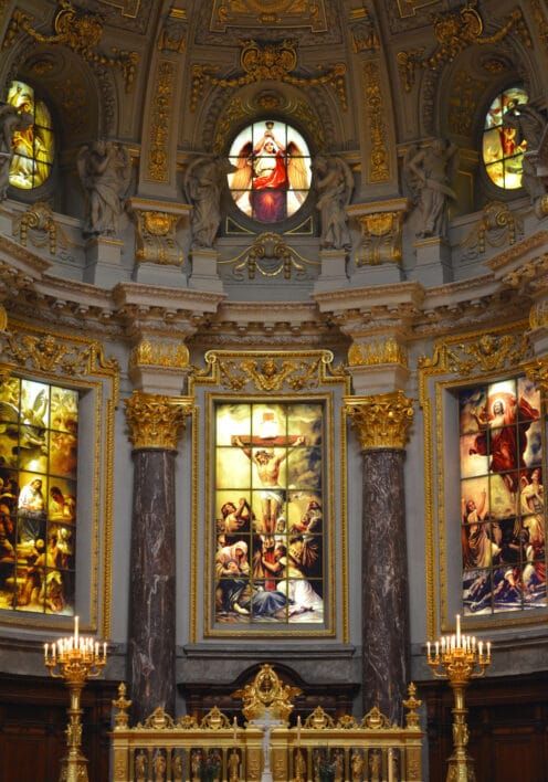 Rephrase More Undo Inside the Cathedral: An altar of gold with gorgeous stained glass depicting bright colours of biblical scenes of a historic European Church interior.