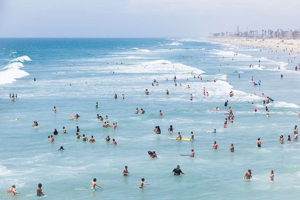 Crowded summer day at Huntington Beach with people swimming, surfing, and enjoying the ocean