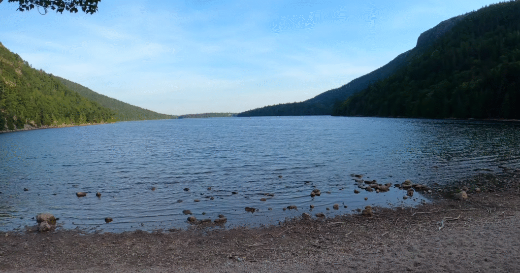 Serene lakeshore surrounded by forested mountains at Acadia National Park, a peaceful spot for walking, photography, and relaxing—one of the many nature activities visitors enjoy when looking for things to do in Acadia National Park