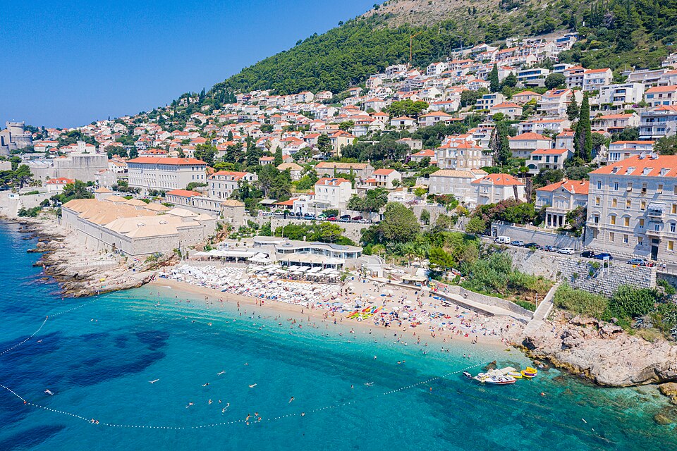 Banje Beach in Dubrovnik with crystal-clear waters and sunbathers, one of the top things to do in Dubrovnik for seaside relaxation and stunning city views