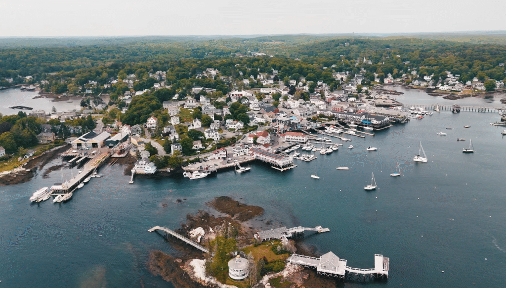 Boothbay Harbor, a picturesque coastal stop along the Portland Maine to Bar Harbor route, showing sailboats, docks, waterfront homes, and lush green scenery surrounding the harbor.