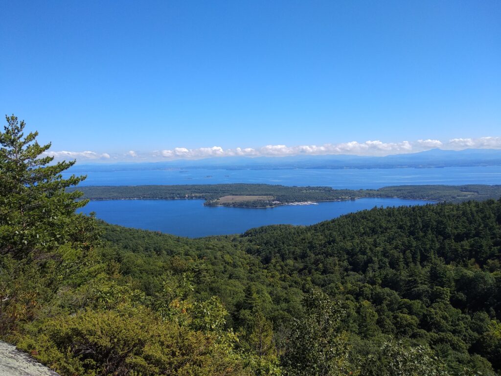 Scenic view of Lake Champlain in Vermont with calm blue water, surrounding green mountains, and a peaceful lakeside atmosphere — one of the best lakes in Vermont for swimming and outdoor activities.