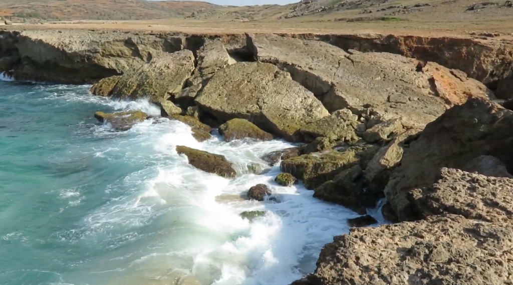 Rocky shoreline and ocean waves crashing against the limestone remnants at the Aruba Natural Bridge collapse site