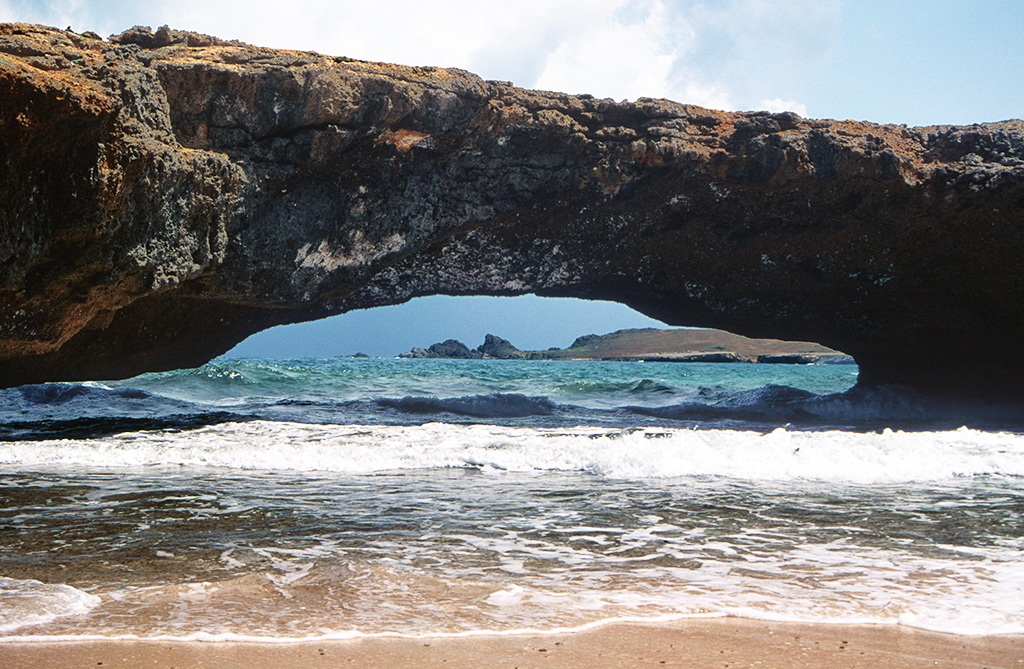 View of the Natural Bridge Aruba with waves crashing beneath the limestone arch along the rugged north coast.