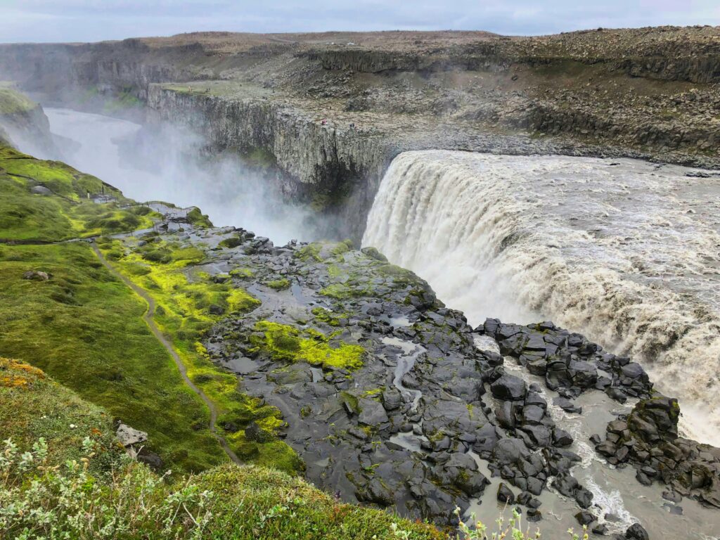Dettifoss waterfall in Iceland with powerful cascading water, basalt canyon cliffs, and vibrant green moss-covered terrain