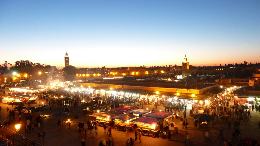 Sunset view of Jemaa el-Fnaa square in Marrakech filled with food stalls, glowing lanterns, and crowds exploring the lively marketplace—an iconic highlight for any Morocco Travel Itinerary.