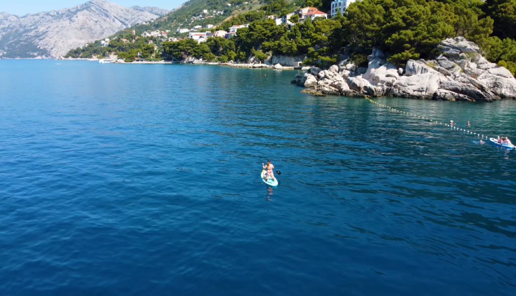 A person paddle boarding on the water at Punta Rata Beach, surrounded by clear blue waves and a sunny sky.