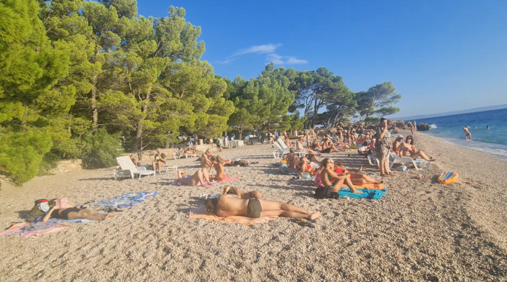 Crowded summer day at Punta Rata Beach in Brela, Croatia, with families relaxing along the beach