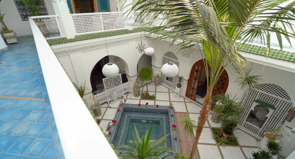 Courtyard view of Riad Malfa Marrakesh with central tiled pool, hanging lanterns, palm trees, and traditional Moroccan architecture
