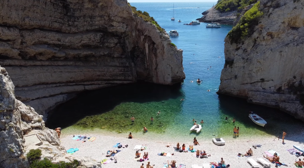 Crowded summer day at Stiniva Beach in Vis, Croatia, with clear water between dramatic cliff walls