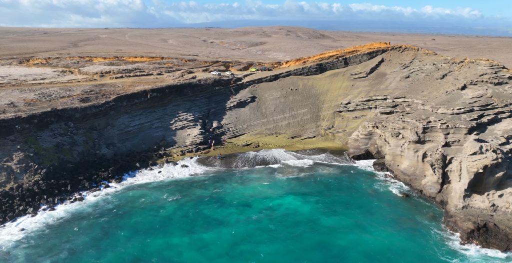 Aerial view of Papakōlea Green Sand Beach on Hawaii’s Big Island featuring turquoise ocean waters, volcanic cliffs, and the unique olive-green shoreline near South Point.