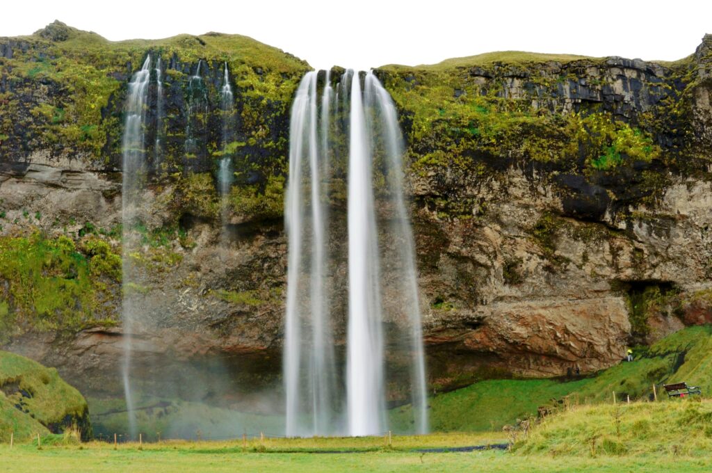 Iceland waterfalls cascading over a moss-covered cliff at Seljalandsfoss, with multiple streams flowing into a green landscape