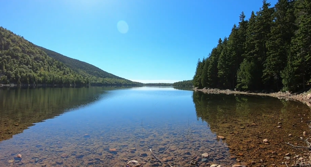 Crystal clear water at jordan pond path trailhead showing rocks on bottom with mountain reflection