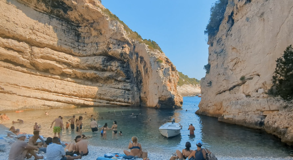 Crowded summer day at Stiniva Beach in Vis, Croatia, with swimmers enjoying the clear water between dramatic cliff walls