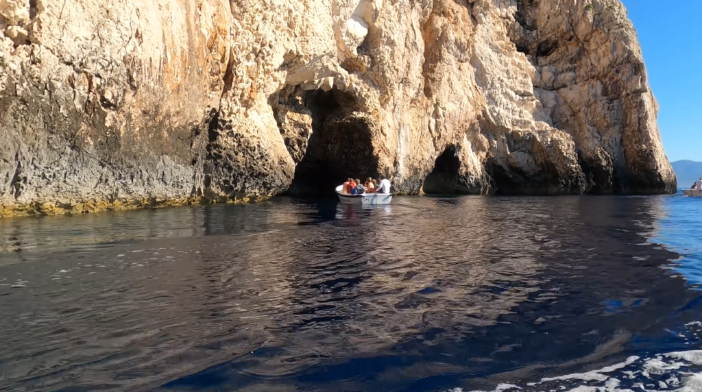 Small boat approaching the rocky cave openings near Stiniva Beach Vis Island, surrounded by rugged cliffs and clear water.