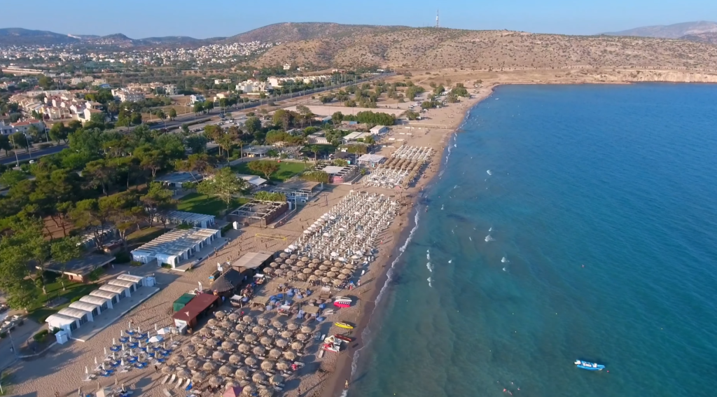 Varkiza Beach Athens showing golden sand, turquoise Saronic Gulf waters, colorful umbrellas, and beachgoers enjoying sunny day