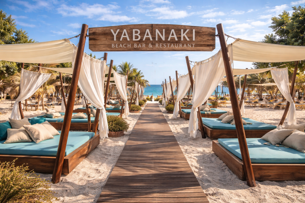 Luxury cabanas and sunbeds at Yabanaki Beach Bar & Restaurant in Greece with a wooden walkway, white curtains, turquoise cushions, and the sea view in the background.